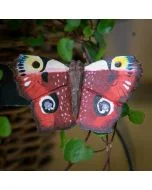 Decoratieve houten vlinder in de vorm van een dagpauwoog, met vier kenmerkende oogtekeningen en donker omrande roodbruine vleugels tussen groene takjes.