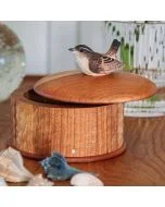 Ronde houten bewaardoos met een bruin winterkoninkje als dekselgreep, gefotografeerd op een houten tafel met decoratieve schelpen.