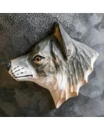 Beschilderde houten wolvenkop als magneet op een grijze metalen wand, met donkere neus, lichtgekleurde hals en zichtbare snijlijnen in de vacht.