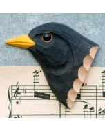 Decoratieve houten vogelmagneet in de vorm van een merel, met helder gele snavel en zwarte veren, liggend op een muziekblad met noten.