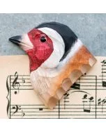 Decoratieve houten vogelmagneet in de vorm van een putter, met opvallend rood gezicht en zwart-witte kop, liggend op een muziekblad.