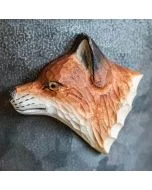 Beschilderde houten vossenkop als magneet op een grijze metalen wand, met amberkleurig oog, donkere oorrand en lichtgekleurde vacht langs de hals.