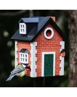 Houten vogelhuis in Engelse cottage-stijl met een koolmees op de zitstok, rode baksteenprint, donkergroene deur en witte ramen tegen een donkere tuinachtergrond.