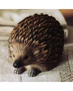 Decoratief houten egelbeeld op een geweven kleed, met een bolle rug vol gesneden stekels, kleine ronde oren en een donkere neus.