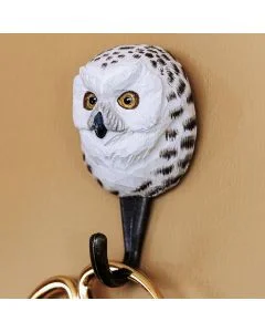 Decoratieve wandhaak met sneeuwuil van hout en metaal tegen een lichte wand