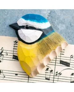 Decoratieve houten vogelmagneet in de vorm van een pimpelmees, met kobaltblauwe kruin, helder gele onderzijde en witte wangen op een muziekblad.