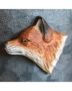 Beschilderde houten vossenkop als magneet op een grijze metalen wand, met amberkleurig oog, donkere oorrand en lichtgekleurde vacht langs de hals.
