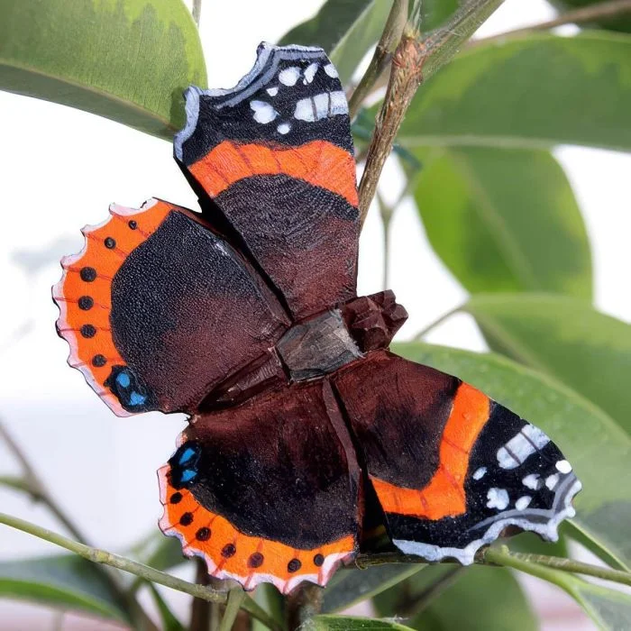 Houten Atalanta vlinder van Wildlife Garden tussen takken en bladeren, met een donkere vleugeltekening, feloranje dwarsbanden en gekartelde vleugelranden.