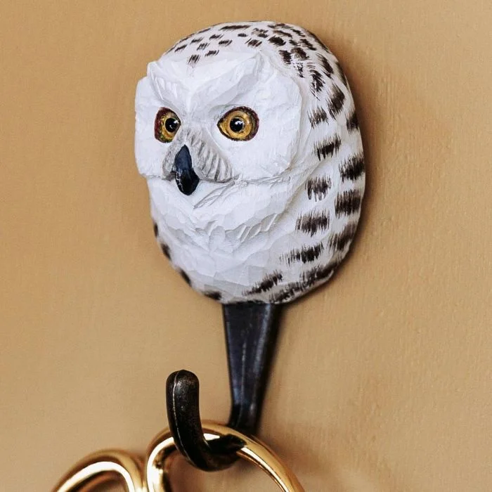 Decoratieve wandhaak met sneeuwuil van hout en metaal tegen een lichte wand