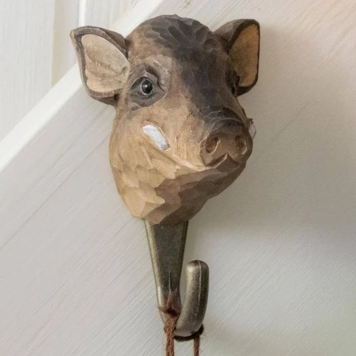 Decoratieve wandhaak met houten wildezwijnkop van Wildlife Garden, bevestigd aan een licht geschilderde wand met een veter aan de haak.