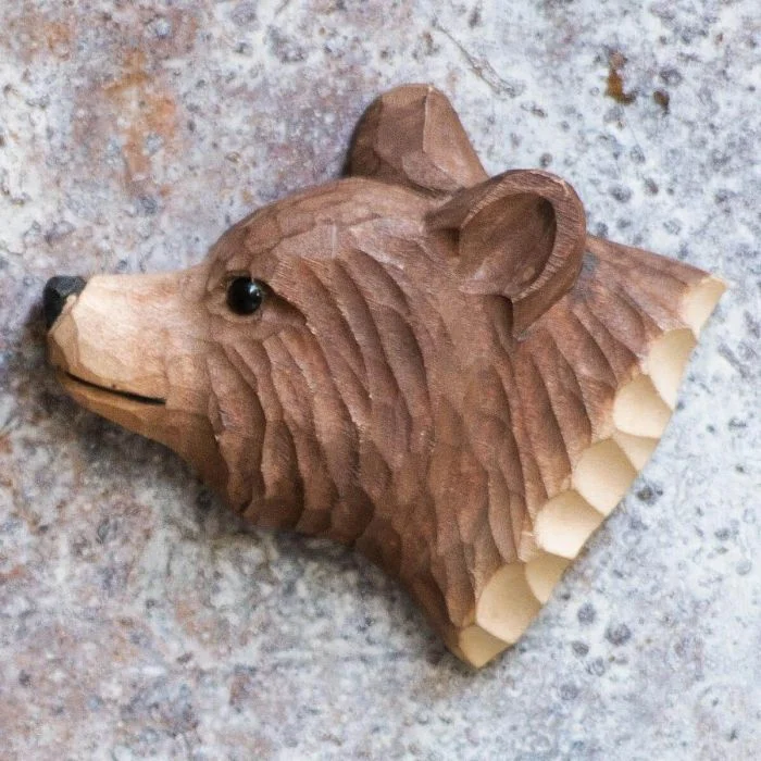 Beschilderde houten berenkop als magneet op een grijs gespikkelde metalen ondergrond, met donkere neus, ronde oorschelpen en gesneden vachtlijnen.