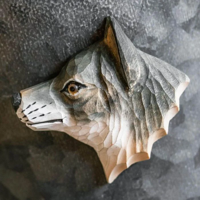 Beschilderde houten wolvenkop als magneet op een grijze metalen wand, met donkere neus, lichtgekleurde hals en zichtbare snijlijnen in de vacht.
