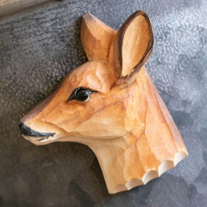 Beschilderde houten reekop als magneet op een donkergrijze metalen wand, met grote oren, zwarte oogpartij en warmbruine vachttekening.